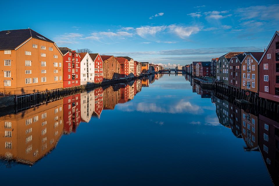 bunte Holzhaeuser am Fluß Nidelva in Trondheim mit Wasserspiegelungen